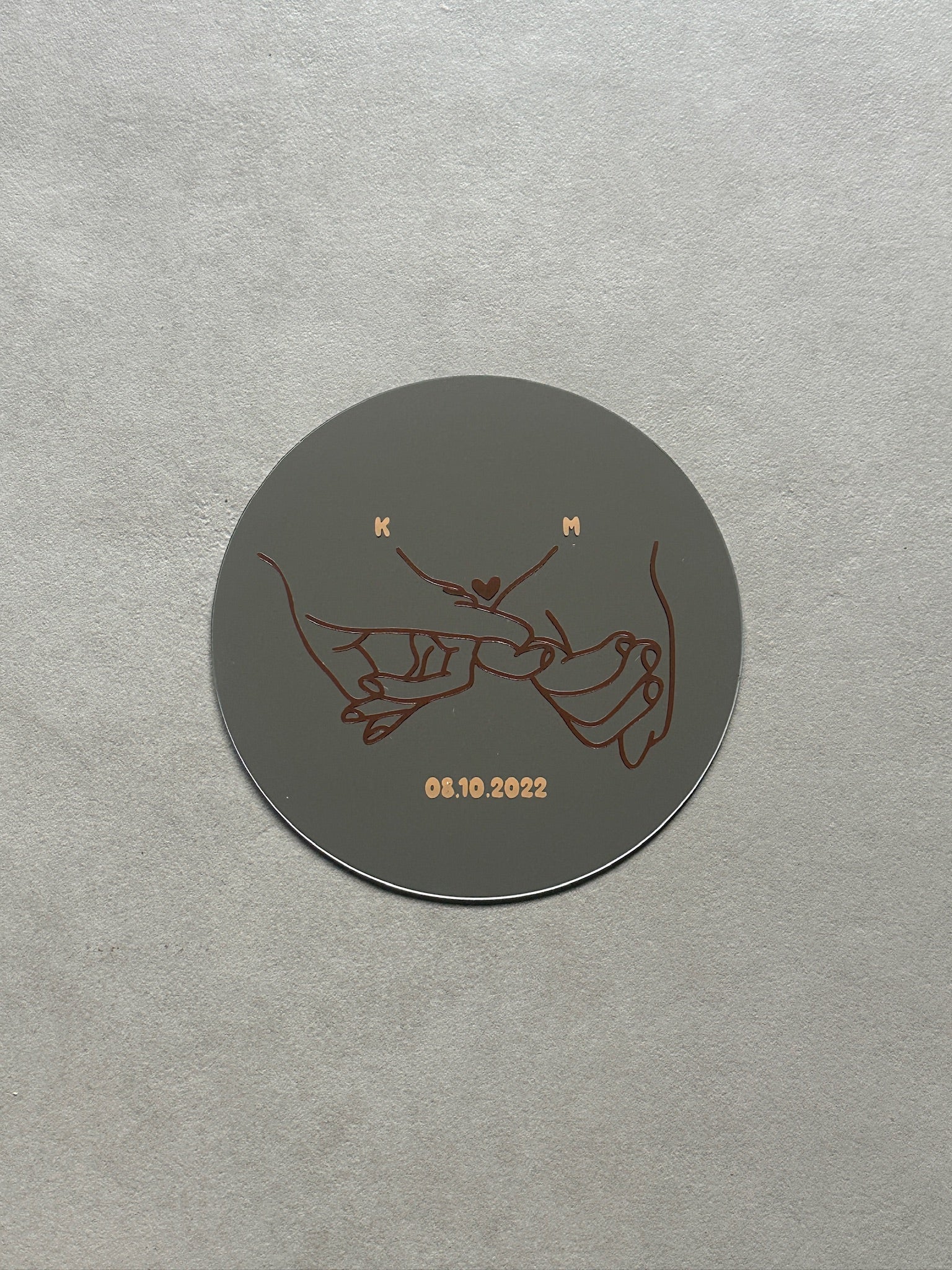 Spiegel met een mannen- en vrouwenhand die elkaars pink vasthouden met daarboven een klein hartje in het bruin. Met datum en eerste letter van namen in caramel 